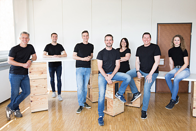 Sieben Personen stehend und sitzend in einem Raum - Das Probando-Team
